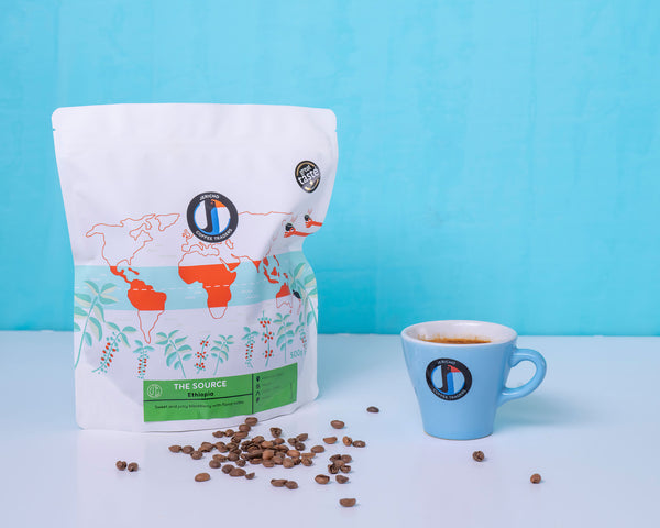 Coffee bag with world map design, coffee beans, and a blue cup on a white surface with a blue background